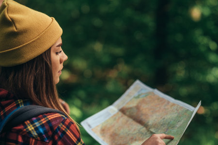 A hiker woman using map for orientation while walking in the forest and wearing backpack with...