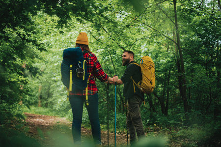 A young couple of hikers using trekking poles and wearing backpacks with camping gear while spending...
