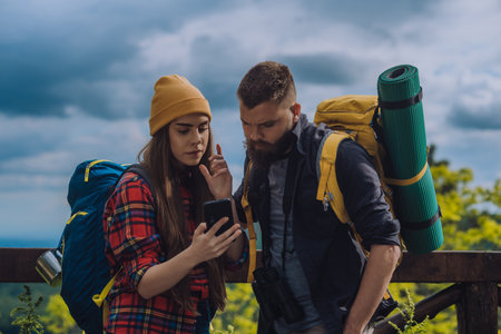 A couple of hikers using a smartphone for orientation when in nature and wearing backpacks with camping gearの写真素材