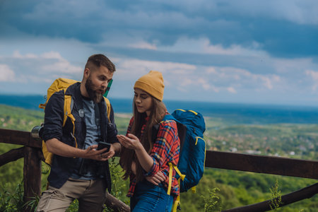 A couple of hikers using smartphone for orientation while spending time in nature and wearing backpacks with a camping gearの写真素材