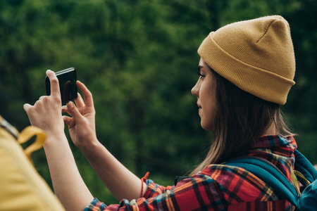 A hiker woman taking picture with a smartphone while walking in the forest wearing backpack with a...