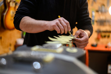 Black electrical guitar in repair service shop with a hands of a guitar luthier which fixes and tightens itの写真素材