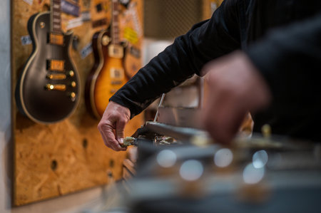 Black electrical guitar in repair service shop with a hands of a guitar luthier which fixes and tightens itの写真素材