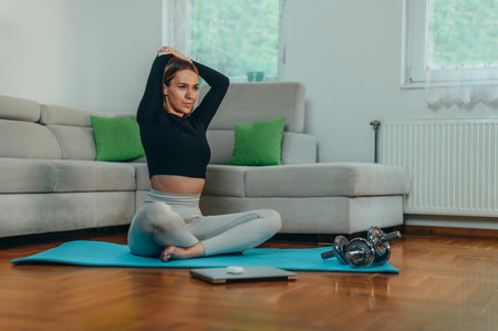 Young attractive woman training at home while using a laptop and sitting on a fitness matの写真素材