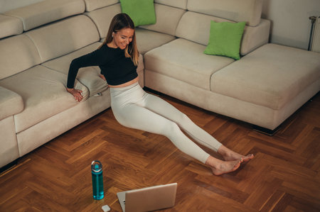 Young attractive woman training at home while using laptop and repeating instructions of an online fitness instructorの写真素材