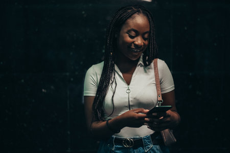 Beautiful african american woman using smartphone while out in the city during nightの写真素材