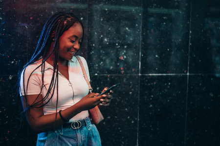 Cheerful african american woman using smartphone while out in the cityの写真素材