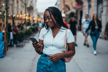 Cheerful african american woman using smartphone while out in the city during the dayの写真素材