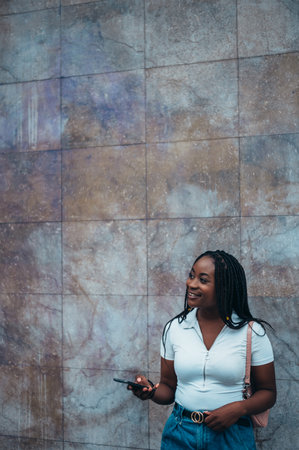 Cheerful african american woman using smartphone while out in the cityの写真素材