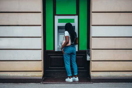 Attractive african american woman using credit card and withdrawing cash at the ATMの写真素材