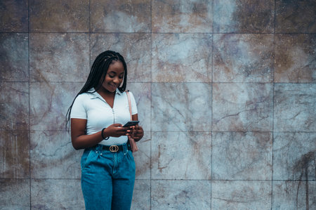 Cheerful african american woman using smartphone while out in the cityの写真素材