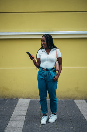 Cheerful african american woman using smartphone while out in the cityの写真素材