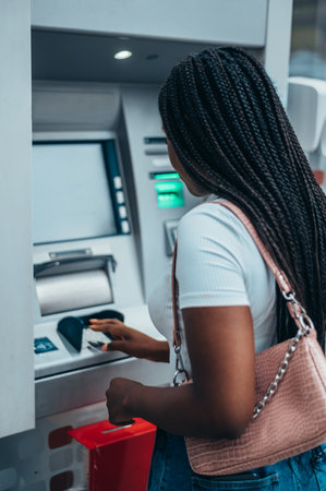 Young african american woman using credit card and atm machine while withdrawing moneyの写真素材