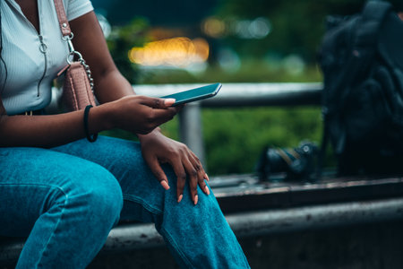 Cheerful african american woman using smartphone while out in the city sitting on a benchの写真素材