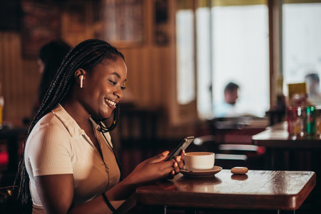 Beautiful young african american woman using smartphone while in a cafe drinking coffeeの写真素材