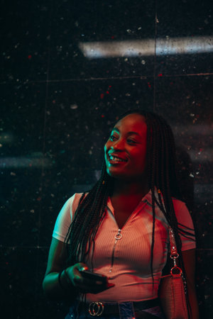 Cheerful african american woman using smartphone while in a subway metro platform at nightの写真素材