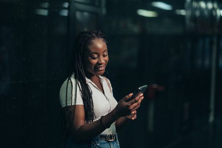 Cheerful african american woman using smartphone while in a subway metro platform at nightの写真素材