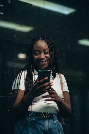 Beautiful african american woman using smartphone while out in city during nightの写真素材