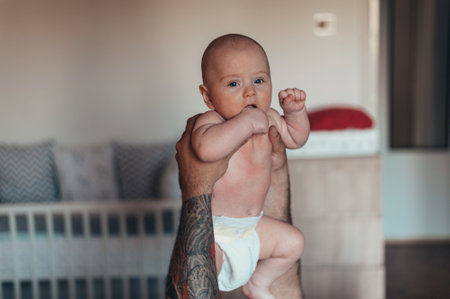 Tattooed bearded father playing with his son in diapers while at home on the bed