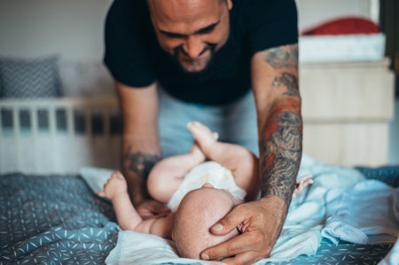 Tattooed bearded father playing with his son in diapers while at homeの写真素材