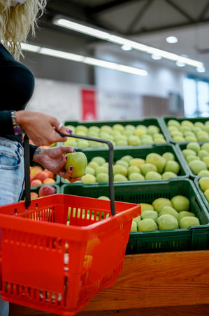 Cropped shoot of a woman in a supermarket choosing products and holding shopping basket while grocery shoppingの写真素材