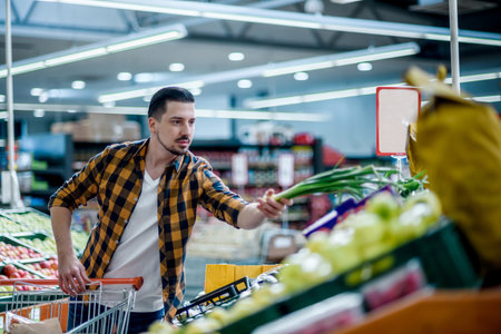 Young handsome man in a supermarket choosing products and holding shopping cart while grocery shoppingの写真素材