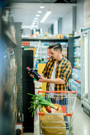 Young handsome man in a supermarket choosing products and holding shopping cart while grocery shoppingの写真素材