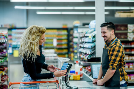 Beautiful woman making a contactless payment with her smartphone at a supermarketの写真素材