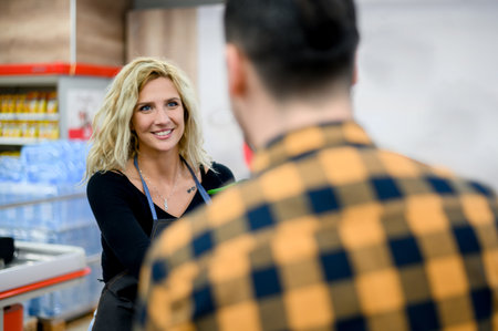 Beautiful young cashier is smiling while working at the supermarket and wearing an apron