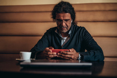 Senior hispanic cuban men using smartphone while sitting in a cafe drinking coffeeの写真素材