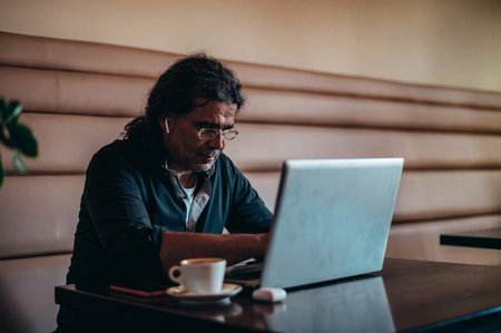 Senior hispanic cuban men using laptop for an video call and having online conference meeting with his colleagues while sitting in a cafeの写真素材