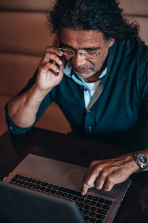 Senior hispanic cuban men using laptop and a smartphone while working remotely in a cafeの写真素材