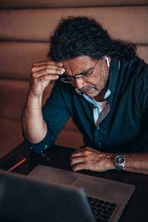 Senior hispanic cuban men using a laptop while having a headache from work stressの写真素材