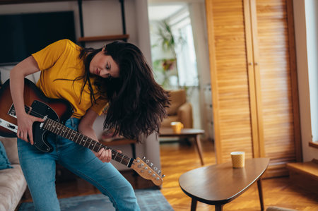 Beautiful young woman playing guitar while dancing and singing in her living room at homeの写真素材