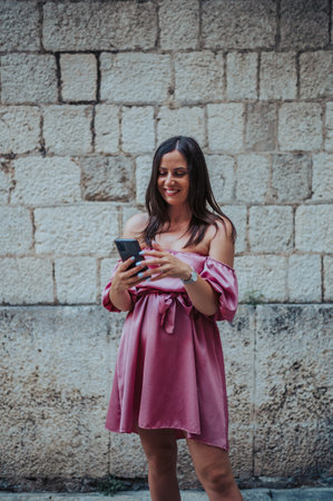 Beautiful young woman using smartphone while walking on the city streets on the coast with a stone...