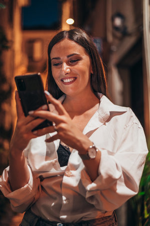 Beautiful young woman using smartphone while walking on the city streets on the coast during the nightの写真素材