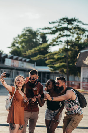 Group of friends taking selfie with a smartphone and drinking beer while having fun at music...