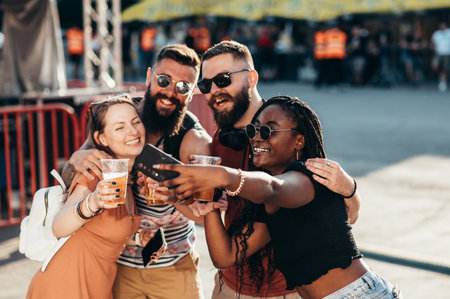 Group of friends taking selfie with a smartphone and drinking beer while having fun at music festivalの写真素材
