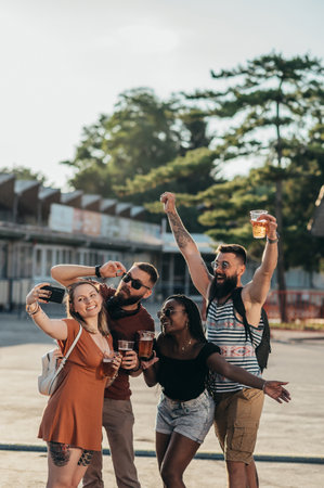 Group of friends taking selfie with a smartphone and drinking beer while having fun at music festivalの写真素材