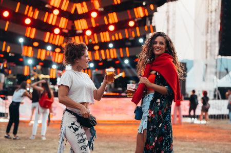 Two beautiful friends drinking beer and having fun on a music festival