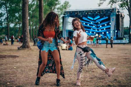 Two beautiful friends drinking beer and having fun on a music festivalの写真素材