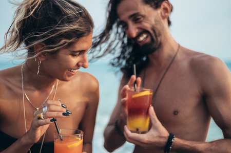 Attractive young couple with alcohol cocktails walking on the beachの写真素材