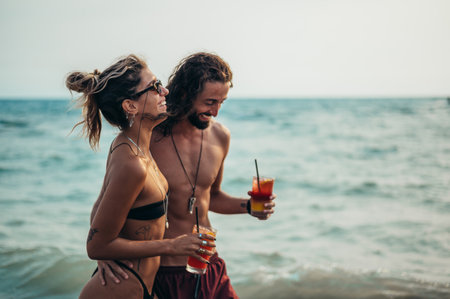 Attractive young couple with alcohol cocktails walking on the beachの写真素材