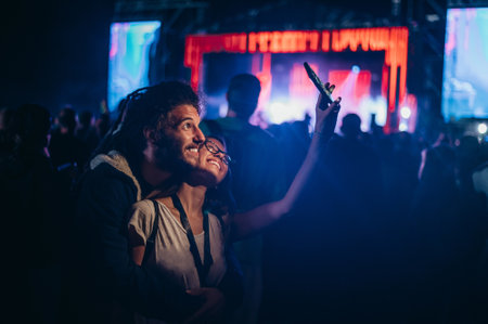 Teenage couple at summer music festival taking selfie with a smartphone while dancing in front of stage. New music entertainment trends. People in love.の写真素材