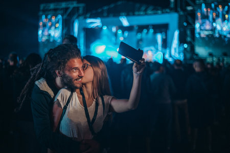 Romantic couple having fun on a music festival and using smartphone while posing for a selfie. Love and celebration concept.の写真素材