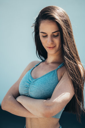 Attractive young woman posing after doing fitness exercises while training outside with a concrete wall in the background and wearing activwearの写真素材
