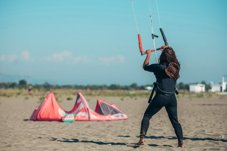 Young sporty woman preparing her equipment for kitesurfing and using flying lines and a control bar while on a sunny beach. Preparation before kiting.の写真素材