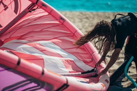 Woman preparing kitesurfing kite with the air pump on a sunny beach. Preparation before kiting.
