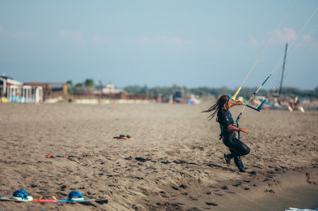Young sporty woman using control bar to lift her kite up in the air and to start kitesurfing. Kitesurfing on a beach.の写真素材