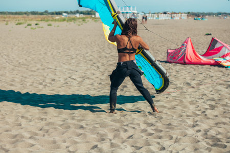 Young sporty woman preparing her kite for kitesurfing and holding it while still on the beach. Preparation before kiting.の写真素材